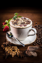 A Cup of coffee with chocolate chips, walnuts, decorated with coffee beans, fresh mint, strawberries and spices star anise.