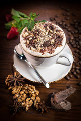 A Cup of coffee with chocolate chips, walnuts, decorated with coffee beans, fresh mint, strawberries and spices star anise.