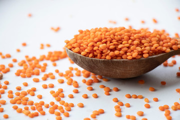 Fototapeta na wymiar Orange lentils on a wooden board. Wooden spoon on a white background. Healthy food, best breakfast.