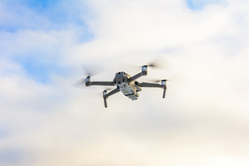 Small gray drone flying in the sky, quadcopter on a cloudy sky background.