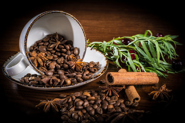 An upturned Cup with scattered coffee beans, decorated with cinnamon sticks, tarragon sprigs and cherries.