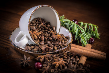 An upturned Cup with scattered coffee beans, decorated with cinnamon sticks, tarragon sprigs and...