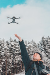 A man launches and removes a small drone or quadcopter on a white background of winter and winter forest.