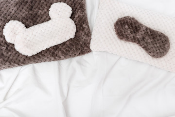 Soft fluffy pillow and sleep mask for eye on white crumpled sheet. Top  view. Flat lay.