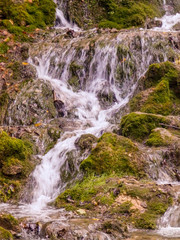 wild landscape with a small waterfall, running water in orange tones. rocks, rocky trees, twigs and moss.