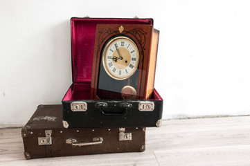 Travel concept. Vintage retro wall clock and old classic leather suitcase on a woodem floor....