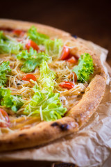 Caesar pizza, with cherry tomatoes, lettuce, Parmesan cheese, crispy crust on a brown background.