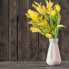 tulips and mimosa in vase on dark wooden background