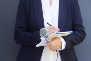 Woman reporter or journalist at media event, holding microphone, writing notes. Broadcast...