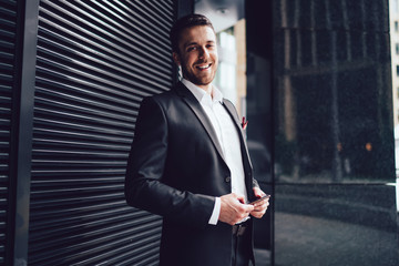 Fototapeta premium Pleasant man in classical suit with smartphone looking at camera with smile in street in downtown