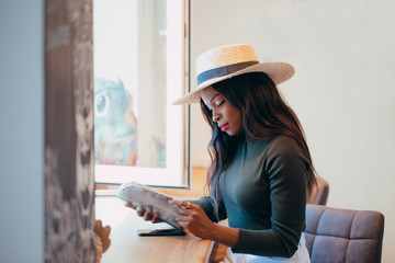 A beautiful young black African girl in white jeans with a happy smile on her face is reading a fashion magazine in a cafe. Fashion colors