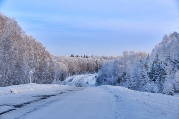 Winter landscape. Winding road through the snowy taiga. Along the edges of the pine, fir and birch are covered with snow. Western Siberia. Salair Ridge. Russia.