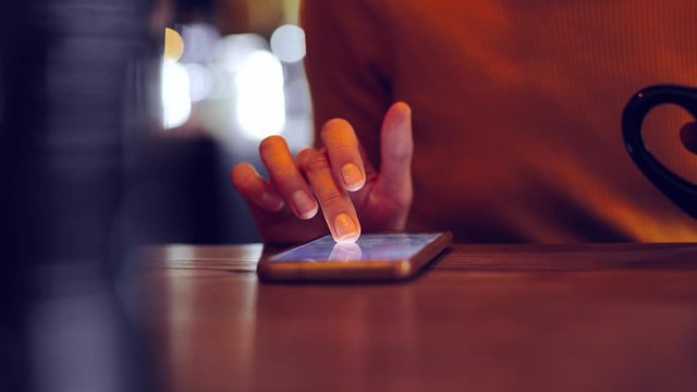 Phone - closeup female hand scrolling using app on smart phone in caffee. Closeup of hand using smartphone indoorsdoors. Mobile cell phone close up.