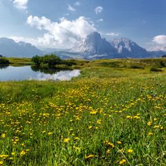 Fototapeta na wymiar Incredible Nature landscape of Dolomites Alps in spring time. Wonderful Mountain valley with fresh green grass, clear lake and majestic Sassolungo peak. Perfect countryside scenery in sunny day.