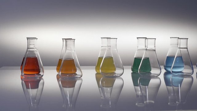 Empty and mixed color liquid filled erlenmeyer flasks reflecting on table