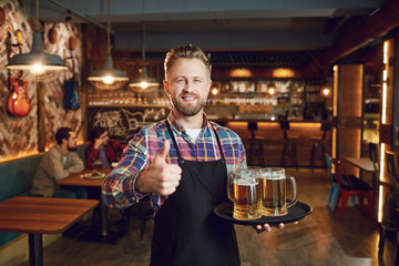 Bearded waiter with a tray of glasses of beer against the background of a pub bar