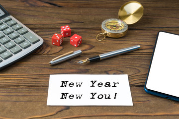 New Year New You written on paper, wooden background desk with calculator, dice, compass, smart phone and pen. Top view conceptual.
