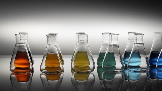 Empty and mixed color liquid filled erlenmeyer flasks reflecting on table