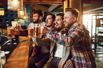 A group of guys watching sports on tv in a pub bar.