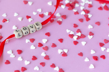 Love text on red ribbon on Wooden cubes on pink background with red and white hearts. Valentines day concept