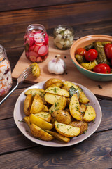 Potato slices baked in the oven with spices on a dark wooden background with pickles