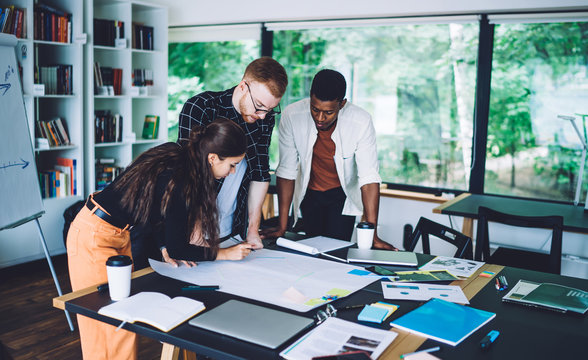 Adult multiethnic colleagues intently working with draft in cozy open space office