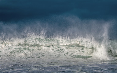 Seascape. Powerful ocean wave on the surface of the ocean. Wave breaks on a shallow bank. Stormy weather, stormy clouds sky background.