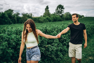 Fototapeta na wymiar A tender loving couple walking in a field of currant. A smiling woman with long hair leads a man, holding his hand