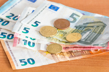 Coins on Euro banknotes on wooden table.