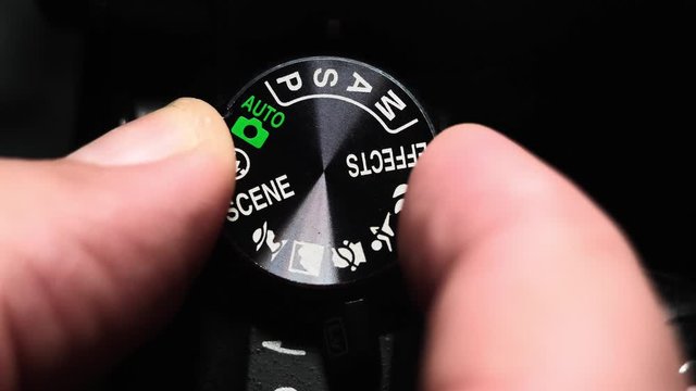 Close-up hands of a male photographer are switching mode on modern digital camera. turn the tuning wheel to manual mode.