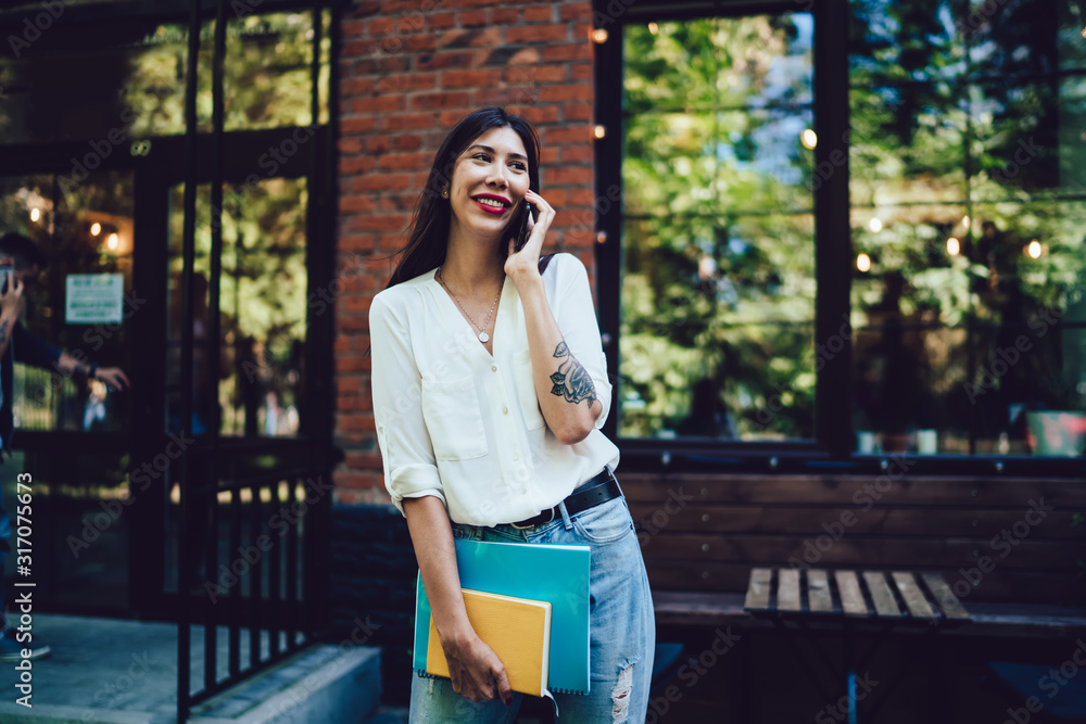 Aufkleber cheerful latino female university student with sketchbook standing at urbanity and using cellphone g