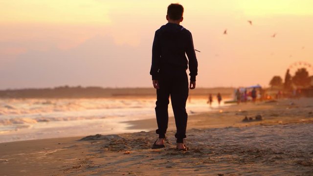 Boy walking at beach on sunset. Boy walking alone on the beach during sunset at seaside