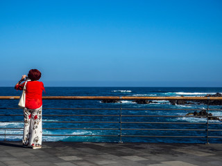 Mujer con blusa roja haciendo fotos con el movil al borde del acantilado