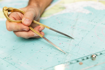 The captain measures the distance on the map with a compass. Close-up.