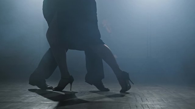 Beautiful man and woman dancing latin dance. Close-up of legs dancing tango in smoky studio in slow motion. 4K, UHD