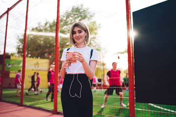 Stylish smiling woman using smartphone in park looking at camera