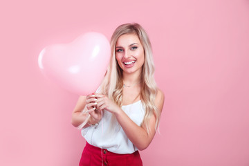 Beautiful young woman with pink heart shape air balloon on color background. Woman on Valentine's Day.