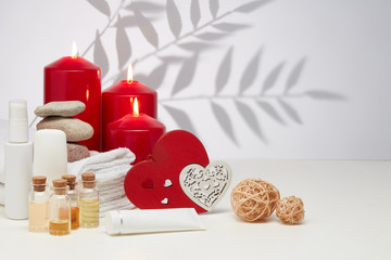 Spa still life with creams, essential oils, candles, hearts on light background. Healthy lifestyle, body care, Valentine's Day.