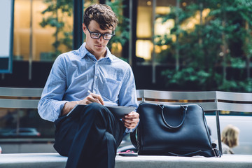 Executive manager in spectacles reading financial news on website on modern touch pad via 4G...