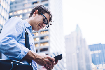 Male worker in shirt and glasses texting on phone at street