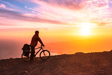 Fototapeta premium Mountain bicycle rider with backpack travels over sunrise background, Lanzarote Canary Island