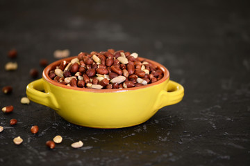Yellow bowl with peanuts on black texture background.