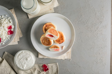 Cheesecakes from cottage cheese with raspberry marmalade on a plate with sour cream and a glass of milk.
