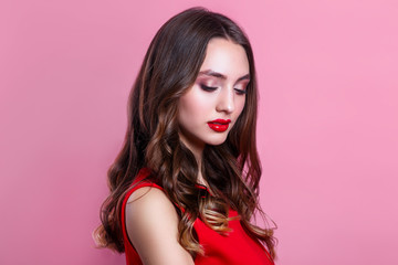 Beautiful woman with red lips, makeup and hairstyle in red dress on pink background