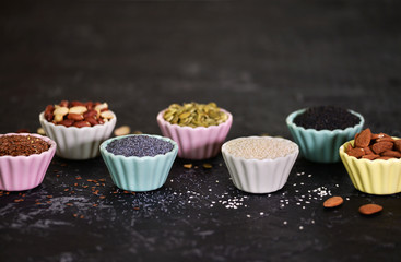Assortment of nuts and seeds in small bowls on a black background.