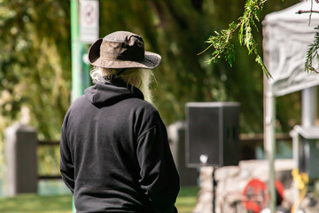 Rear view of female wearing brown sun hat and black hoodie while standing during sunny day against speaker and tree at park