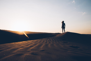 Fototapeta premium Woman walking in desert at sunset