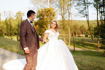 Just married loving hipster couple in wedding dress and suit on green field in a forest at sunset. happy bride and groom walking running and dancing in the summer meadow.