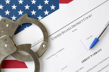 District Court Arrest Warrant court papers with handcuffs and blue pen on United States flag....