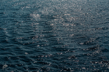 Background of transparent blue sea water top view. Water ripples and pattern on ocean surface with sunlight reflection.